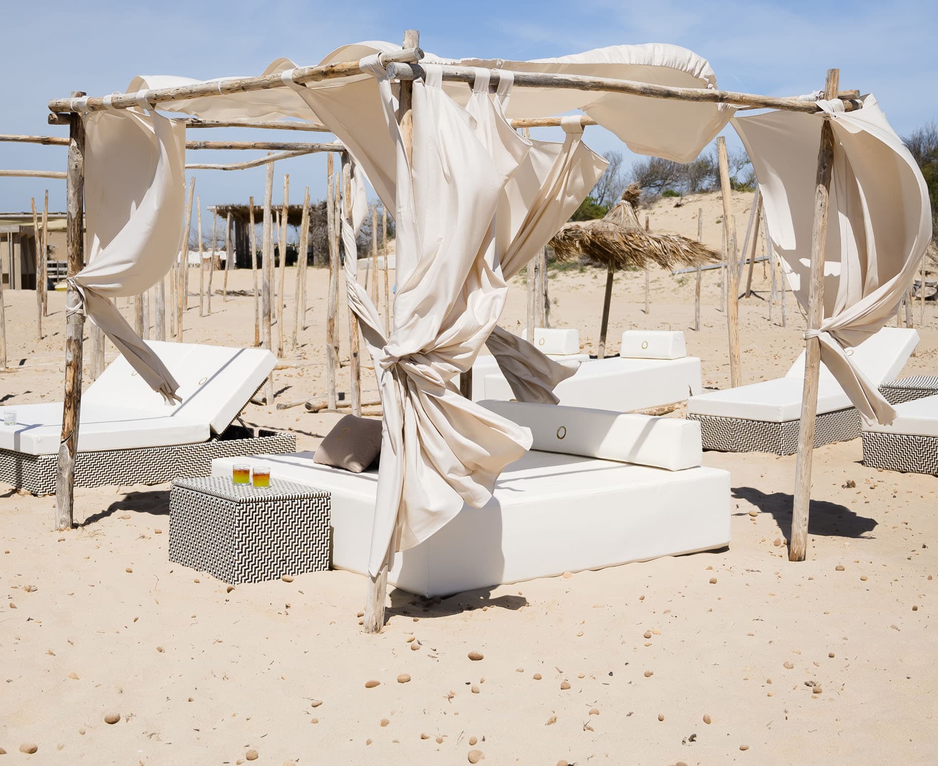 Pura Vita Beach: lettini bianchi sotto baldacchini di lino sulla sabbia.